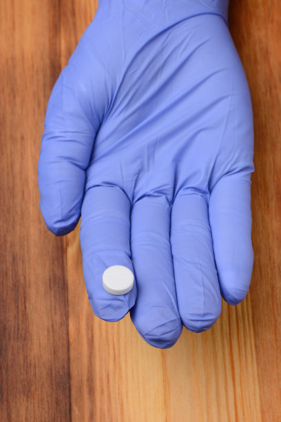 手拿医用手套，拿出一粒药抵着木质纹理图片下载