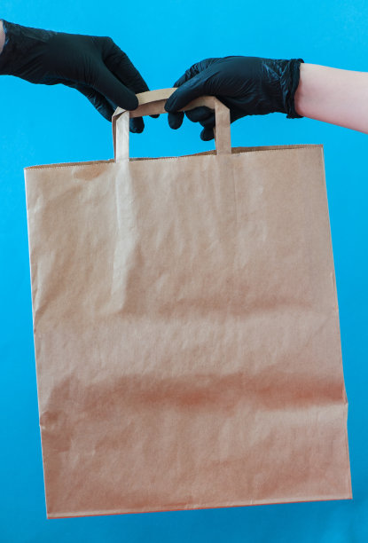 裁剪的手与黑色手套紧握工艺纸袋。图片下载