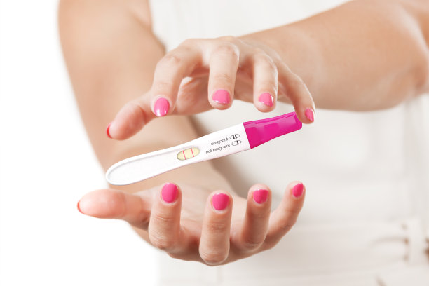 两个女人的手保护阳性塑料怀孕测试。图片下载