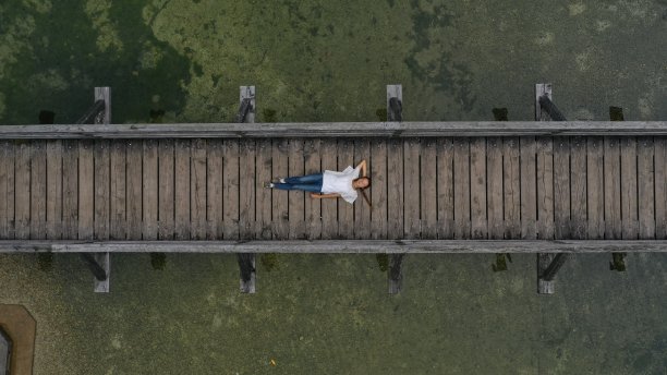 从空中俯视，年轻女子躺在木桥上，越过山河，池塘。哈尔斯塔特,奥地利图片下载