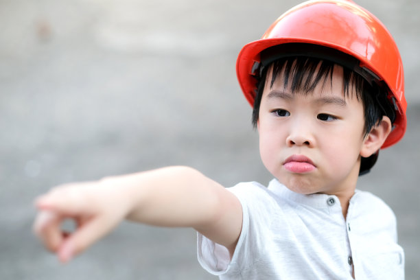 年轻的亚洲男孩身穿灰色T恤，戴着橙色安全帽，站在自家花园的阳光下图片下载