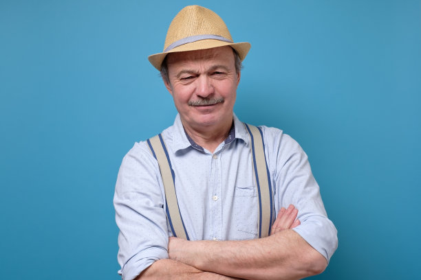 严肃的老男人戴着夏天的帽子，双手交叉摆姿势。图片下载