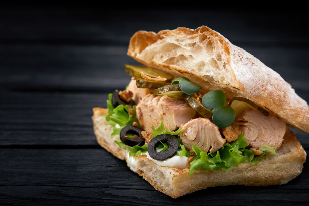 美国快餐。多汁的金枪鱼三明治与奶酪，沙拉和橄榄在黑暗的背景。俱乐部的食物图片下载