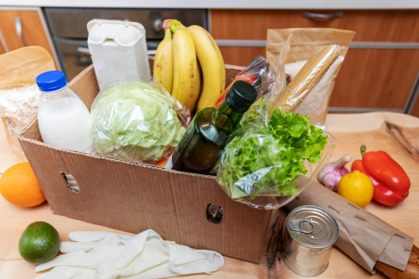 新鲜的食品在纸板箱和木制桌子和保护手套。安全的交付。食物捐赠。有选择性的重点。图片下载