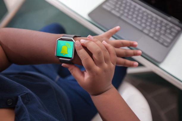 一名坐在课桌前的学生通过看手表上的闹钟来踱步和管理时间。图片下载