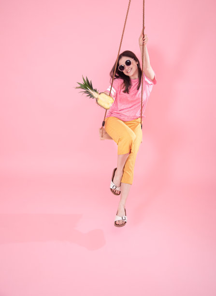 年轻女子在粉红色的背景下荡秋千。图片下载