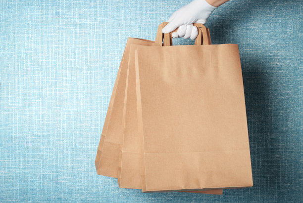一个戴着白手套的女人手里拿着三个纸板袋子，背景是蓝色的，是送餐的概念图片下载