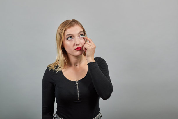 女孩在黑色夹克灰色背景时尚女人拉睫毛从眼睛图片下载
