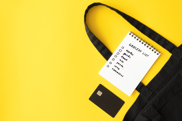 购物清单在纸记事本，棉花生态黑色购物袋和信用卡在黄色背景与副本空间，俯视图。概念网上购买产品，水平图片下载