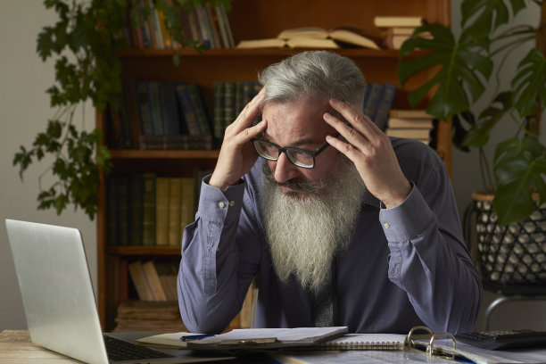 远程教育的概念。累得心烦意乱的导师看着笔记本电脑，抓着自己的头，选择性的集中注意力图片下载
