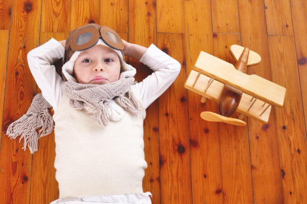 一个女孩在她的卧室里，打扮成飞行员或飞行员，玩着她的木制飞机，她睁着眼睛梦想着，思考着未来。图片下载
