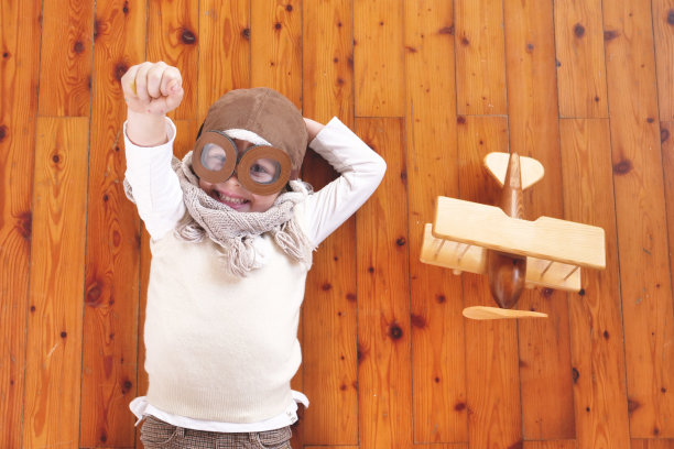 一个女孩在她的卧室里，打扮成飞行员或飞行员，玩着她的木制飞机，她睁着眼睛梦想着，思考着未来。图片下载