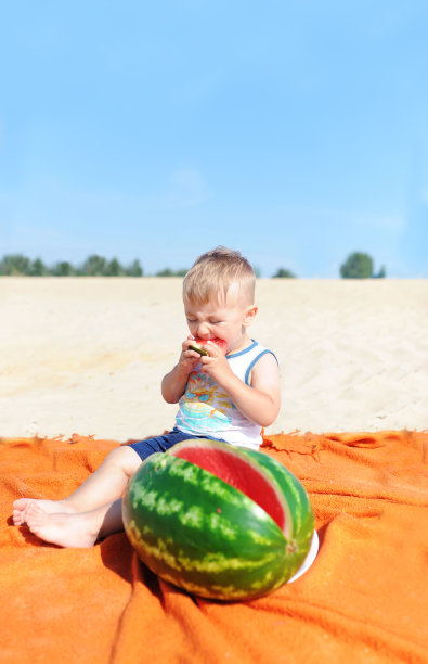 小男孩在沙滩上吃西瓜片图片下载