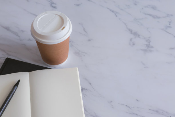 棕色的纸杯咖啡，黑色的书，课本或日记，白色的大理石桌子上有复印空间。品牌和标志的照片概念，咖啡馆，休闲，阅读，放松。餐饮形象。图片下载