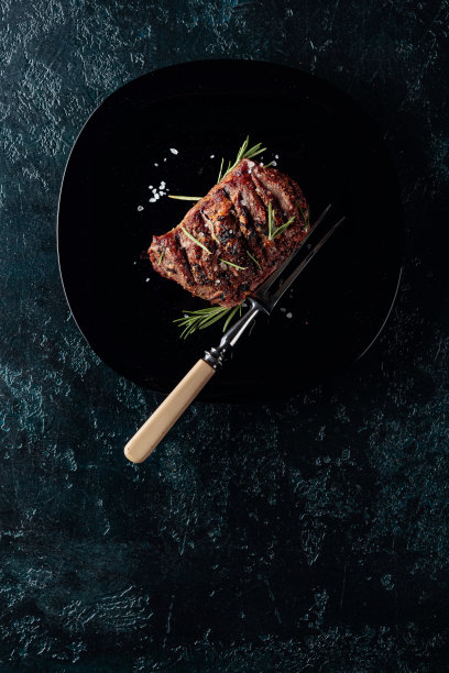 烤肋眼牛排配迷迭香和盐在黑盘子上。图片下载