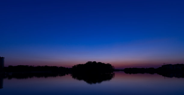长曝光雄伟的景观剪影岛和地平线森林背景风景视图在黄昏夜晚环境的深蓝色照明后日落，平滑的湖泊水面前景图片下载