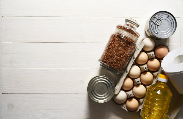 食物捐赠在一个白色的木制背景:油，荞麦，鸡蛋，罐头食品。坐在家里。隔离。食品交付。图片下载