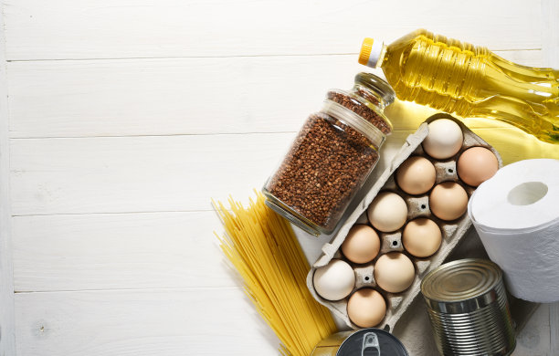 食物捐赠在一个白色的木制背景:油，荞麦，鸡蛋，罐头食品。坐在家里。隔离。食品交付。图片下载