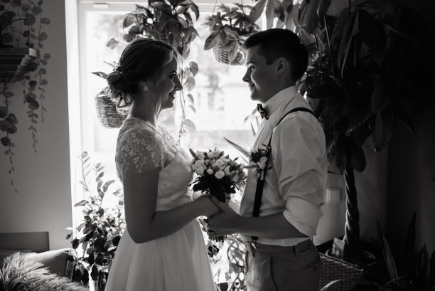 婚礼当天，手捧花束在窗前对视的幸福新人（黑白照片）图片下载