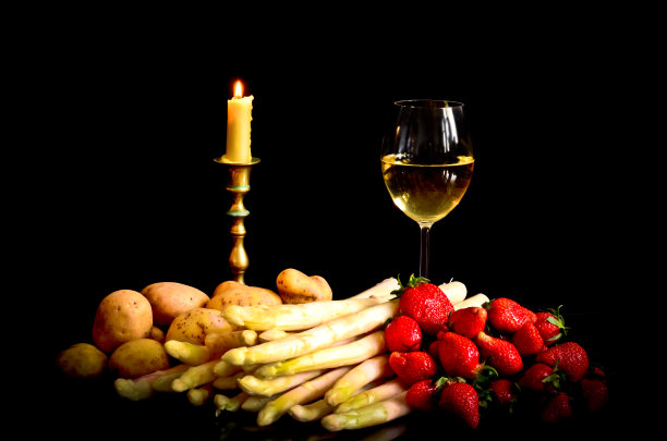 生芦笋、土豆和草莓摆在黑色的背景前，配上一杯葡萄酒、一个罐子和一支蜡烛，像一幅静物画，像一幅古代艺术家的画图片下载