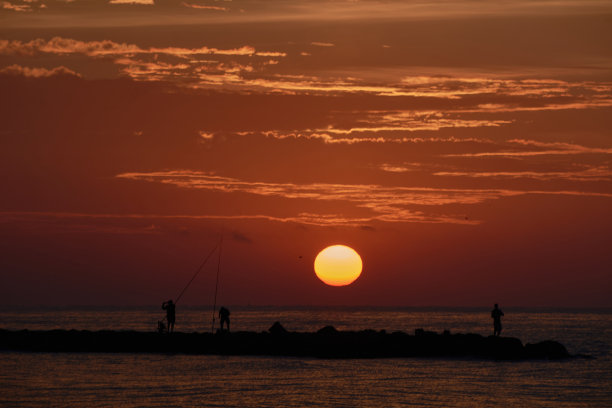 太阳出现在防波堤上的渔民中间图片下载