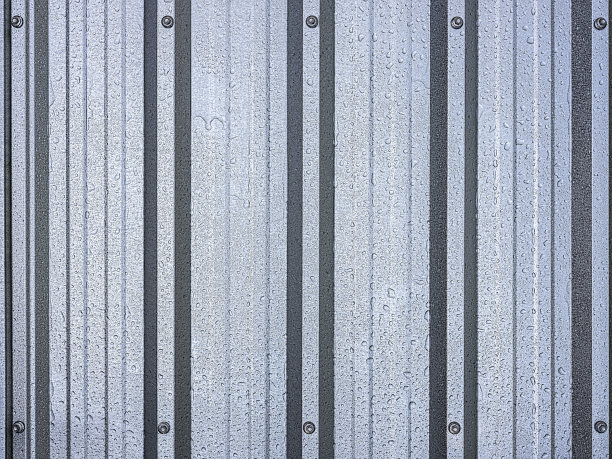 雨后的镀锌金属湿屋顶板作为背景，显示脊形轮廓的纹理，在图像的顶部和底部边框的中心。图片下载