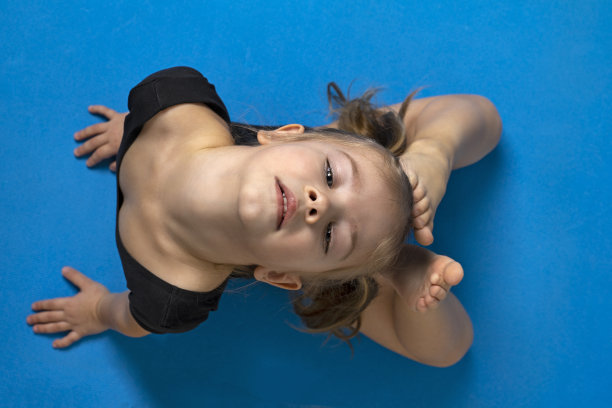 小女孩穿着黑色体操紧身衣在蓝色体操垫上做运动圈，俯视图图片下载