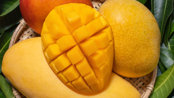 芒果，热带水果，在竹木筛篮上以绿叶为背景，顶视图，全框，美观，成熟的收获设计理念。图片下载