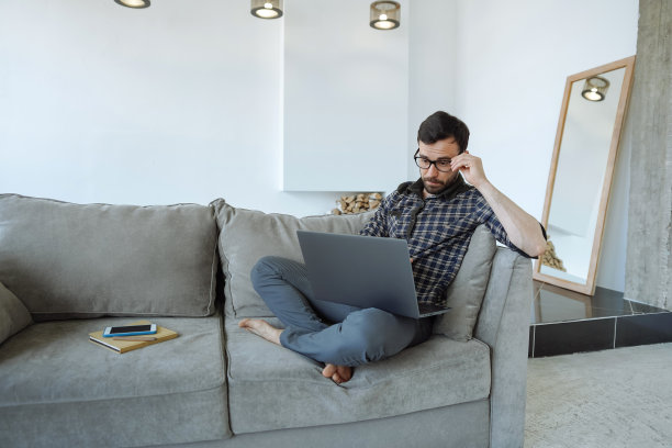 一个带着笔记本电脑坐在沙发上的困惑男人图片下载