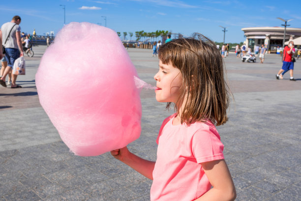 在一个阳光明媚的夏日，一个女孩在户外吃棉花糖。图片下载