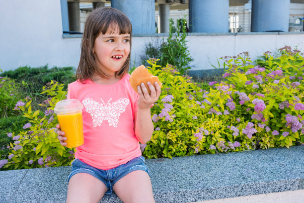 一个小女孩拿着芝士汉堡和橙汁的肖像。快餐。图片下载