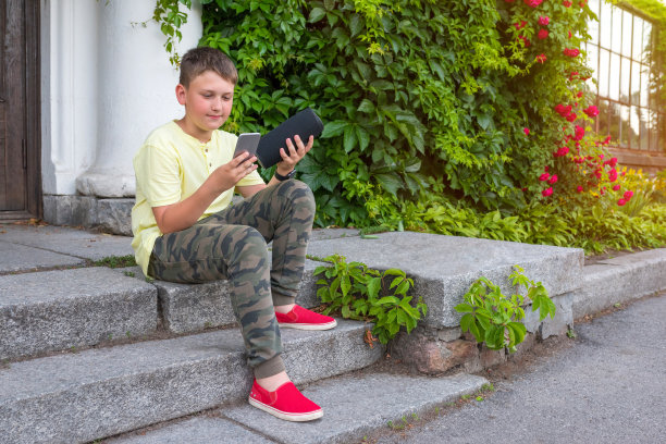 在一个阳光明媚的日子里，一个男孩坐在街上，手里拿着一个手机，拿着一个音乐专栏。金色的小时。图片下载