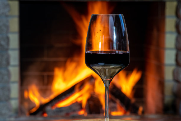 在乡村别墅舒适的壁炉前喝一杯红酒。图片下载