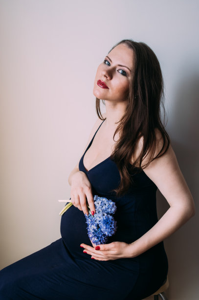 一名身穿深蓝色连衣裙的孕妇，手里拿着一束鲜花图片下载