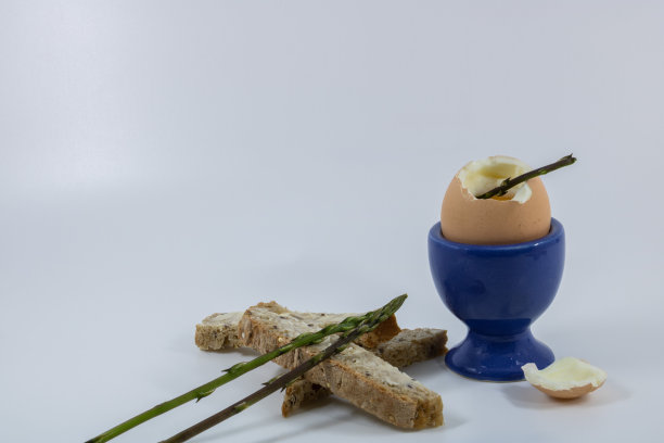 煮鸡蛋在它的蓝色蟑螂和面包屑烤黄油粗Guérande盐以及野生芦笋照片在白色的背景与文字空间图片下载