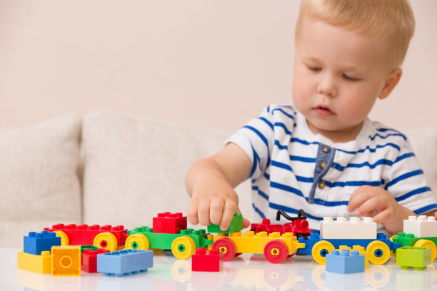 蹒跚学步的小男孩在桌子上玩五颜六色的塑料砖。蹒跚学步的孩子有乐趣和建筑明亮的构造砖。早期的学习。条纹背景。开发的玩具图片下载