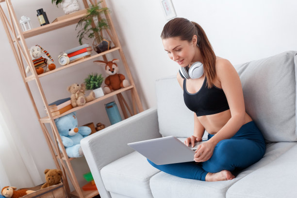 瘦削健康的运动女孩在打底裤，健身顶部坐在荷花姿势在沙发上拿着笔记本电脑在脚上。看起来有用的创意信息，饮食，排毒健康食谱。聊天的朋友，可爱，关心图片下载