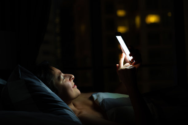 睡在床上的女孩在看智能手机。睡觉前查看新闻和社交网络。聪明的小玩意。图片下载