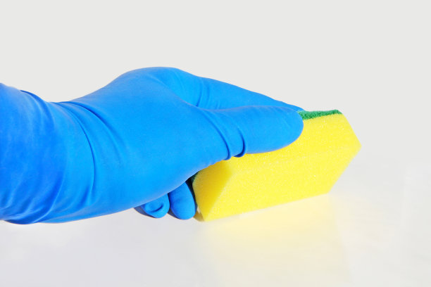 手在蓝色橡胶手套与黄色清洁海绵的特写。图片下载