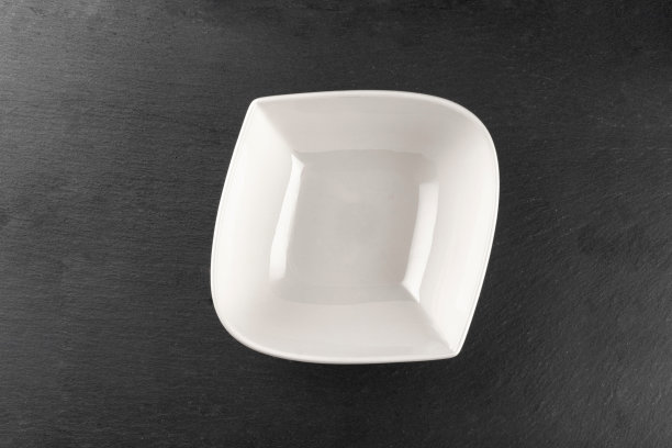 盘子孤立在石头上。黑色背景上的方形白色空盘子。清洗圆瓷陶器。早餐餐具。图片下载