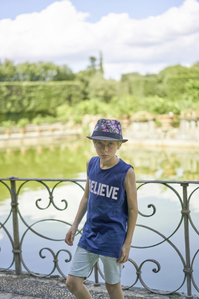 一个年轻英俊的十几岁的男孩戴着一顶夏天的帽子站在湖边，怀疑地看着摄像机图片下载