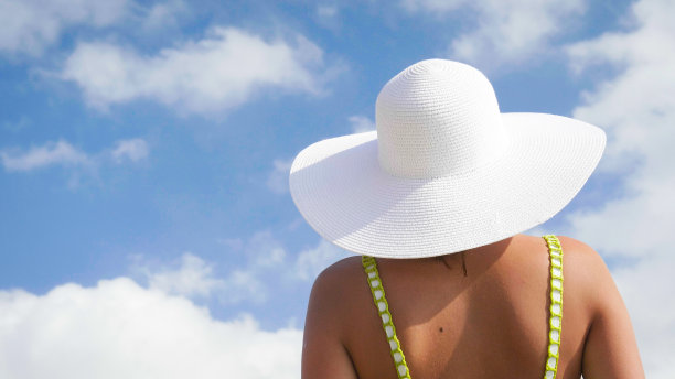 一个漂亮的年轻女孩在海边散步，穿着泳衣，戴着草帽。图片下载