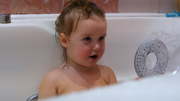美丽的小女孩在浴缸里摆姿势，浴缸里有水和泡沫，做鬼脸图片下载