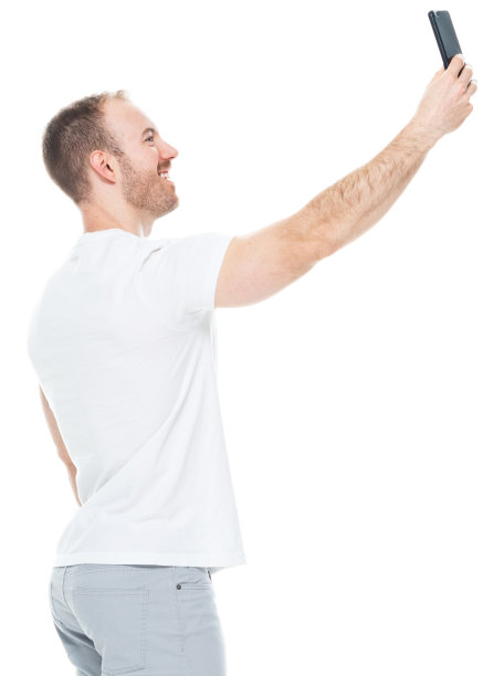 白人年轻男性穿着裤子站在白色背景前用手机拍照图片下载