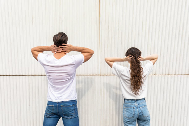 一对夫妇双手抱头站在一堵白色墙壁前的后视图图片下载