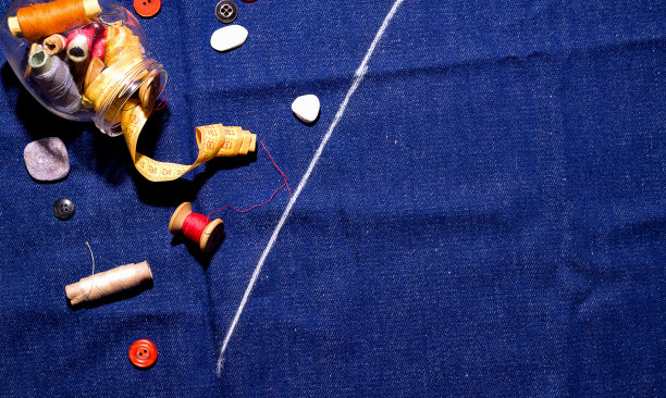 家庭缝纫的概念。蓝色牛仔布上的一罐线和纽扣。副本的空间。图片下载