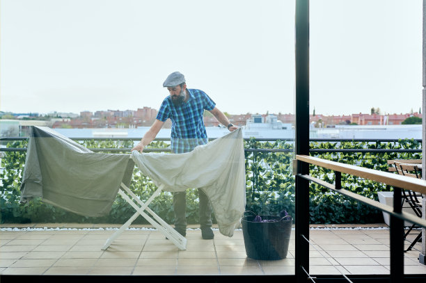 从一扇大窗户看到一个留着胡子戴着帽子的中年男子在阳台上挂着床单图片下载