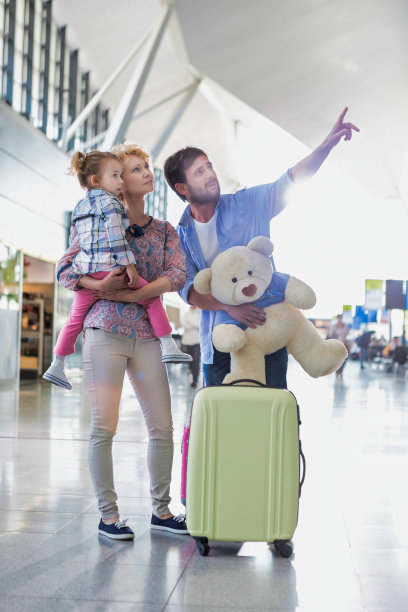 一个快乐的家庭在假日看着他们的航班在机场的监视器与镜头光晕图片下载