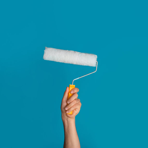 重新装饰房子。千禧男子拿着滚筒刷在蓝色的背景，特写素材图片