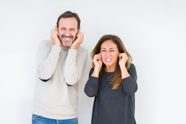 美丽的中年夫妇在孤立的背景下相爱，用手指捂住耳朵，因为大声的音乐噪音而烦恼的表情。聋的概念。图片下载